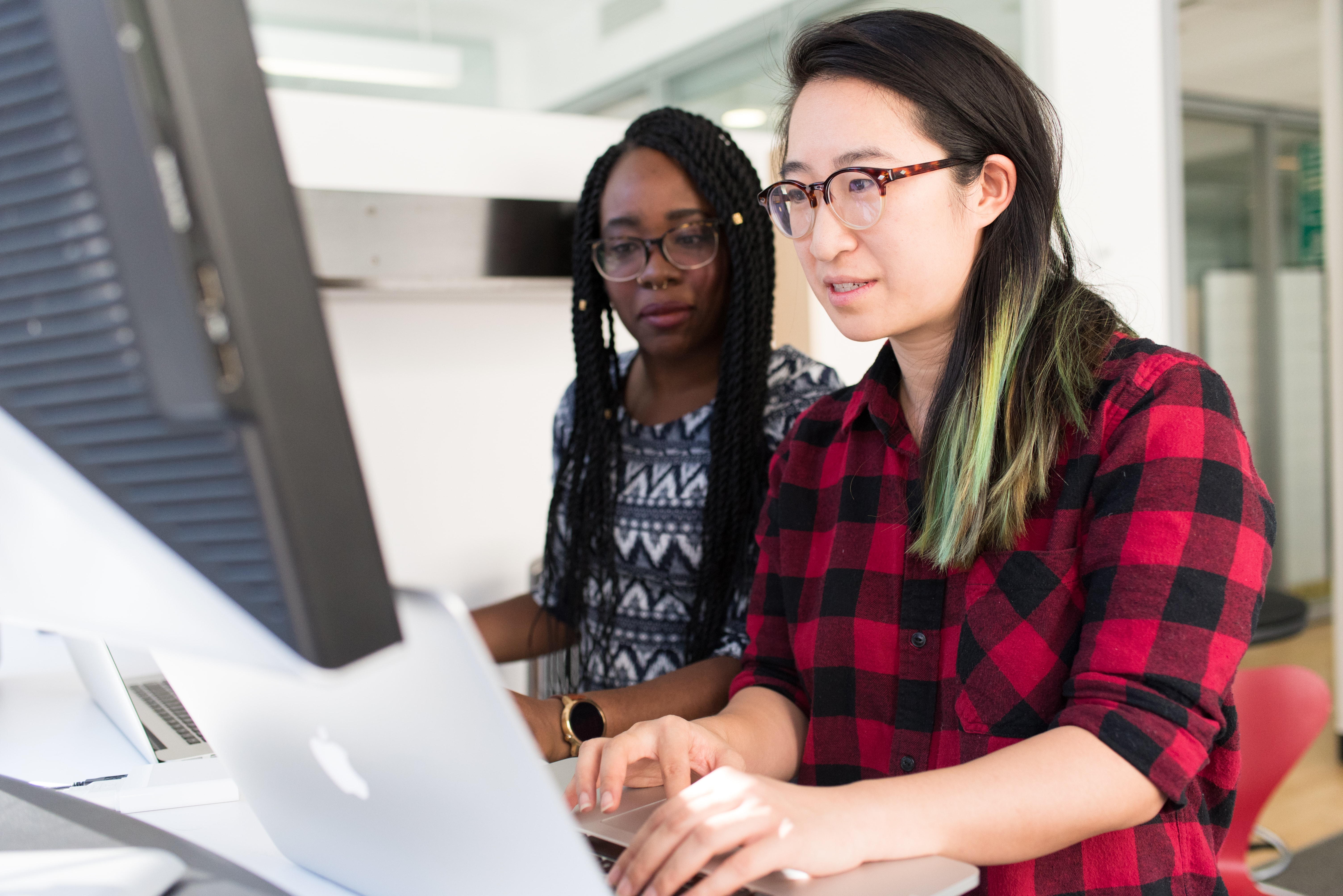 Dos mujeres con lentes observando una computadora y un monitor